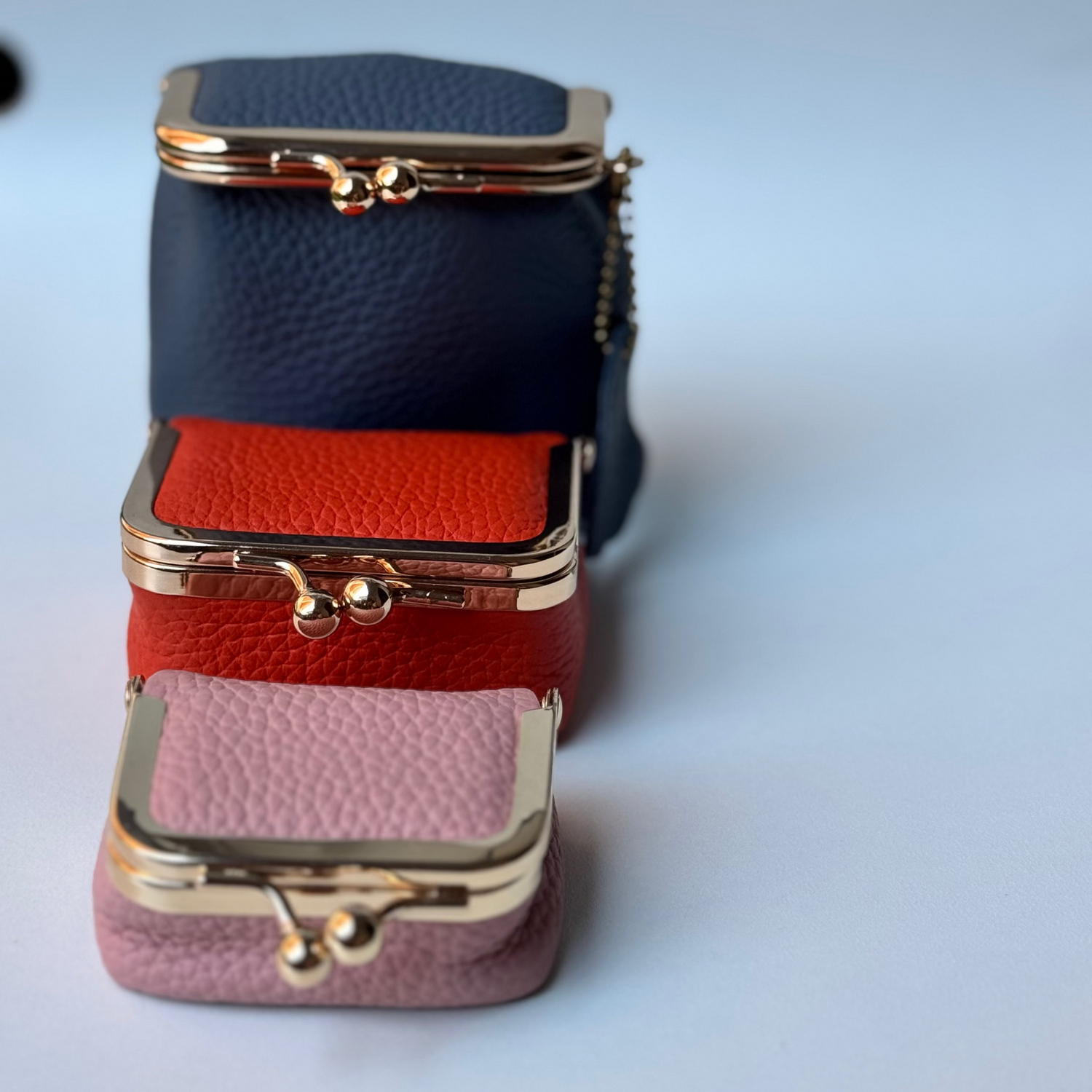Three small leather pouches stacked on a light blue background